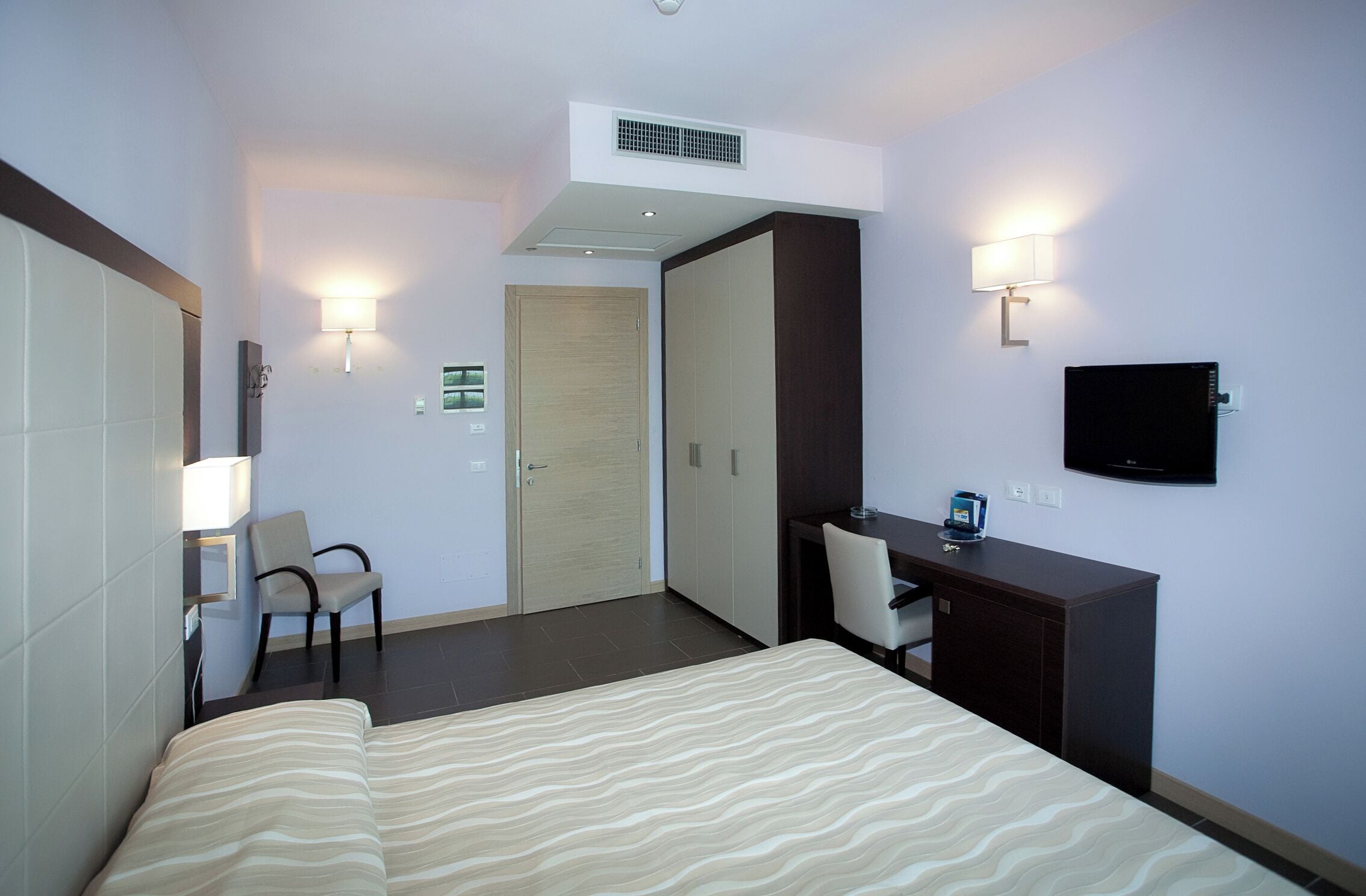 A hotel room with a bed, desk, chair, wardrobe, and a television.