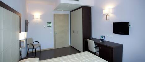 A hotel room with a bed, desk, chair, wardrobe, and a television.