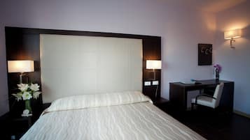 Een hotelkamer met een groot bed, twee bedlampen, een bureau met stoel, en een kleine vaas met bloemen.