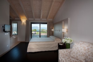 A hotel room with a bed, a sofa, a TV, a window with curtains, and a view of the outdoors.