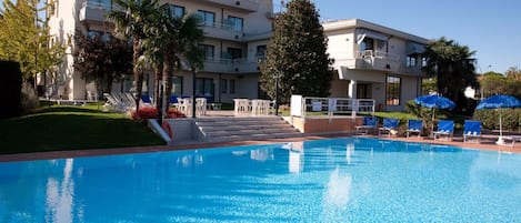 Un hôtel doté d’une piscine, de palmiers et de chaises longues.