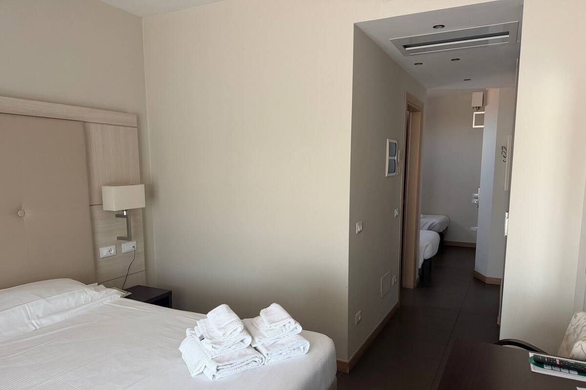 Quarto de hotel com cama, mesa de cabeceira, luminária e toalha dobrada sobre a cama.