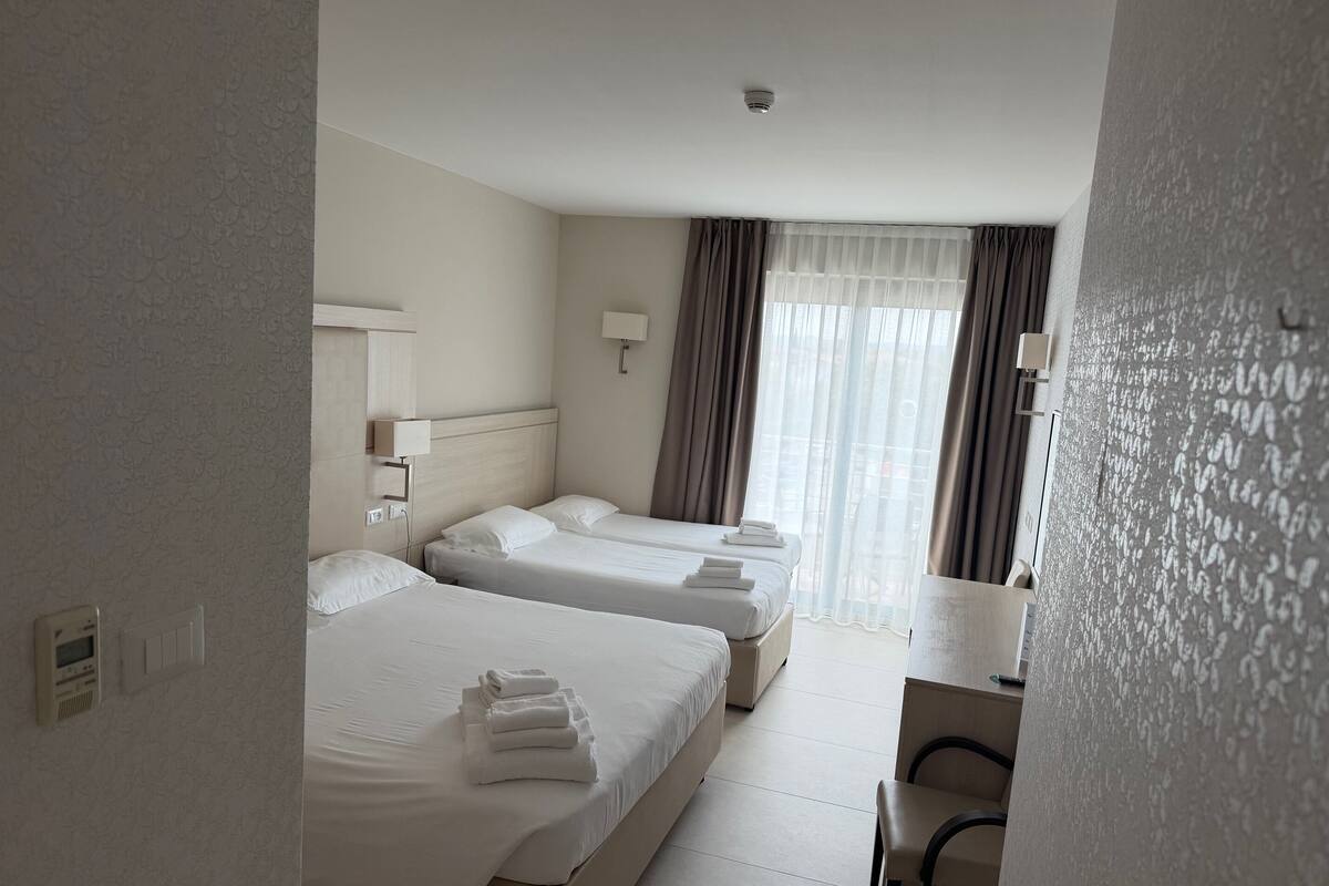 Quarto de hotel com duas camas, uma mesa e uma janela com cortinas.