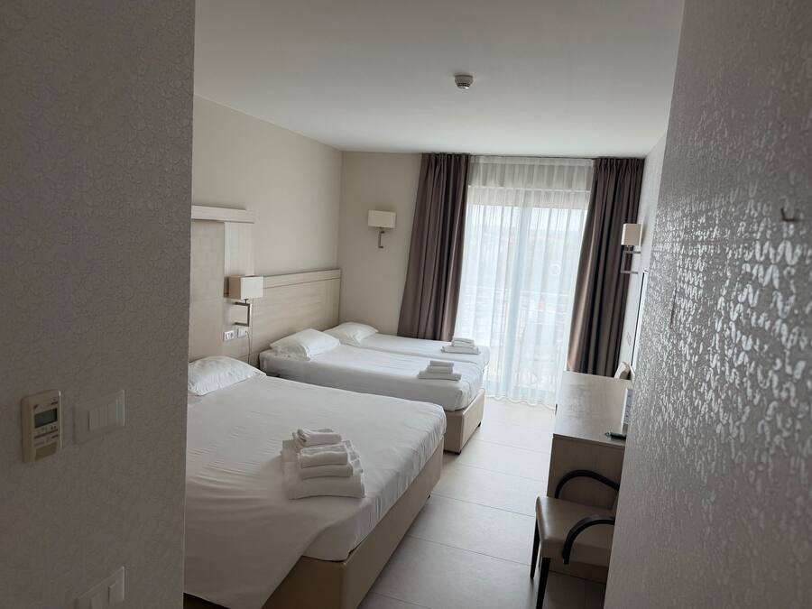 Een hotelkamer met twee bedden, een bureau en een raam met gordijnen.