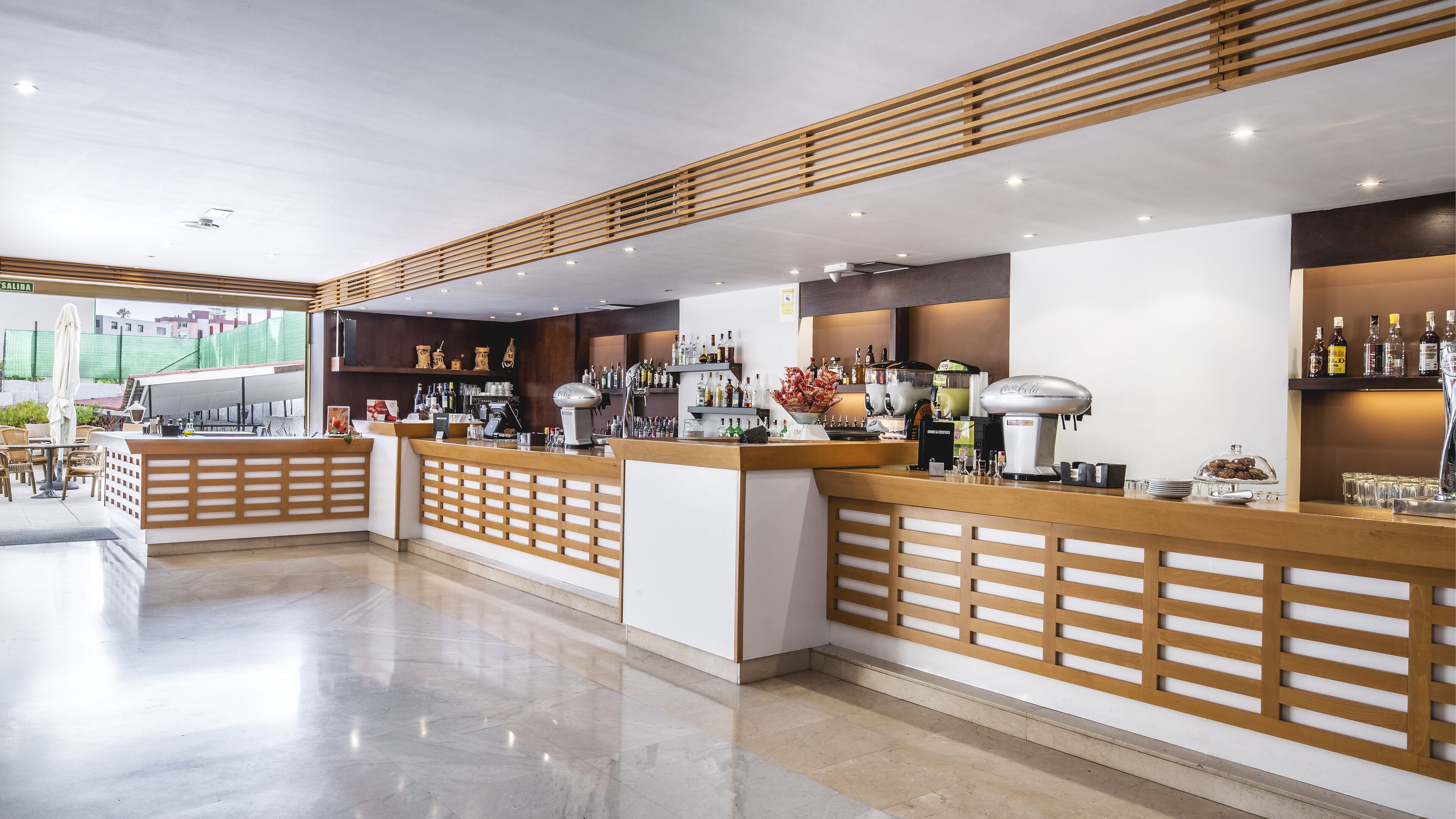 A modern bar area with wooden counters, a variety of liquor bottles, and a coffee machine.