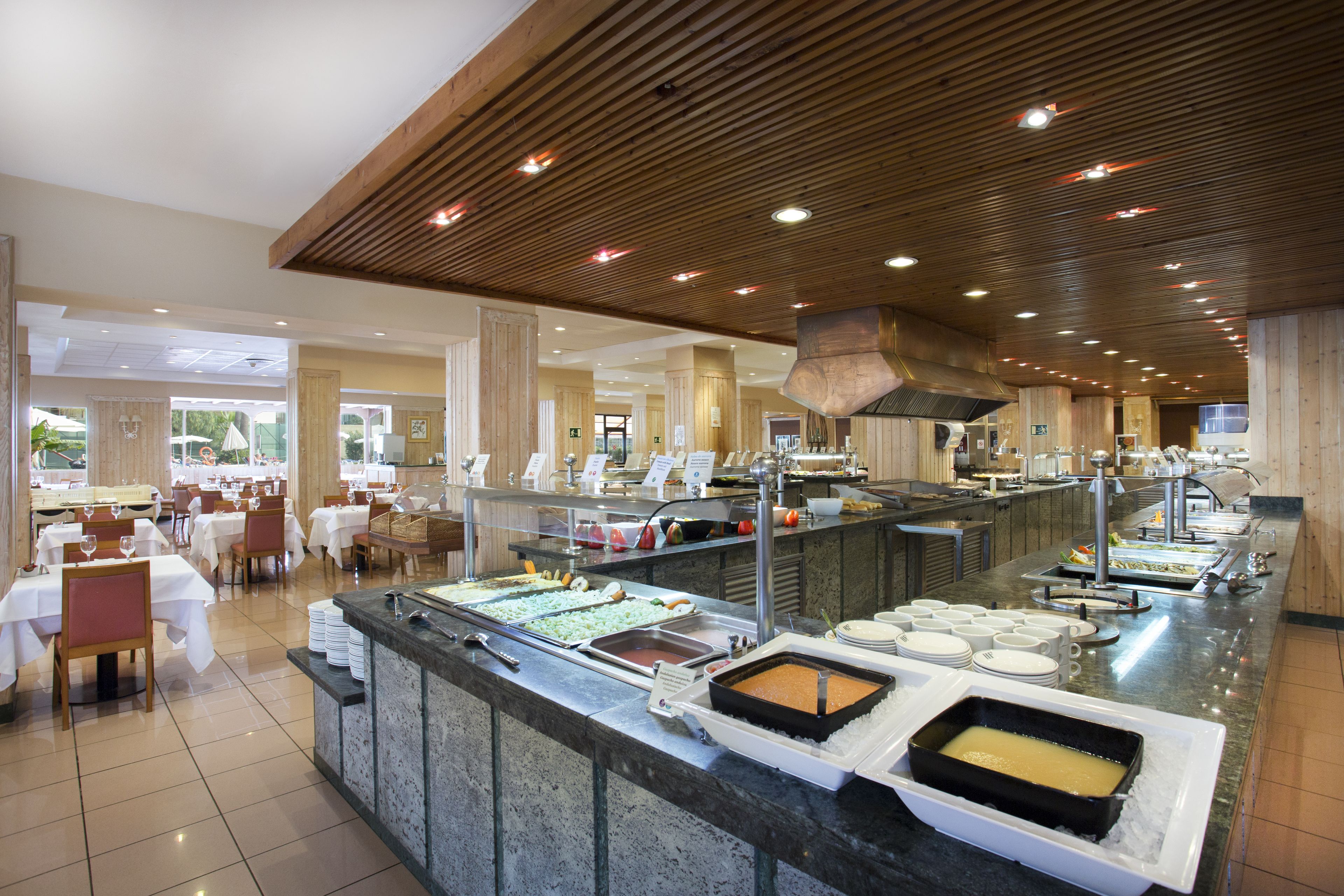 Zona de buffet con distintas estaciones de comida, mesas con sillas y una decoración interior moderna.