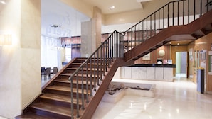 Un moderno vestíbulo de hotel con una escalera de madera, suelos de mármol y un mostrador de recepción.