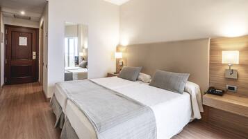 A hotel room with a large bed, bedside lamps, a nightstand with a phone, and a wooden headboard.