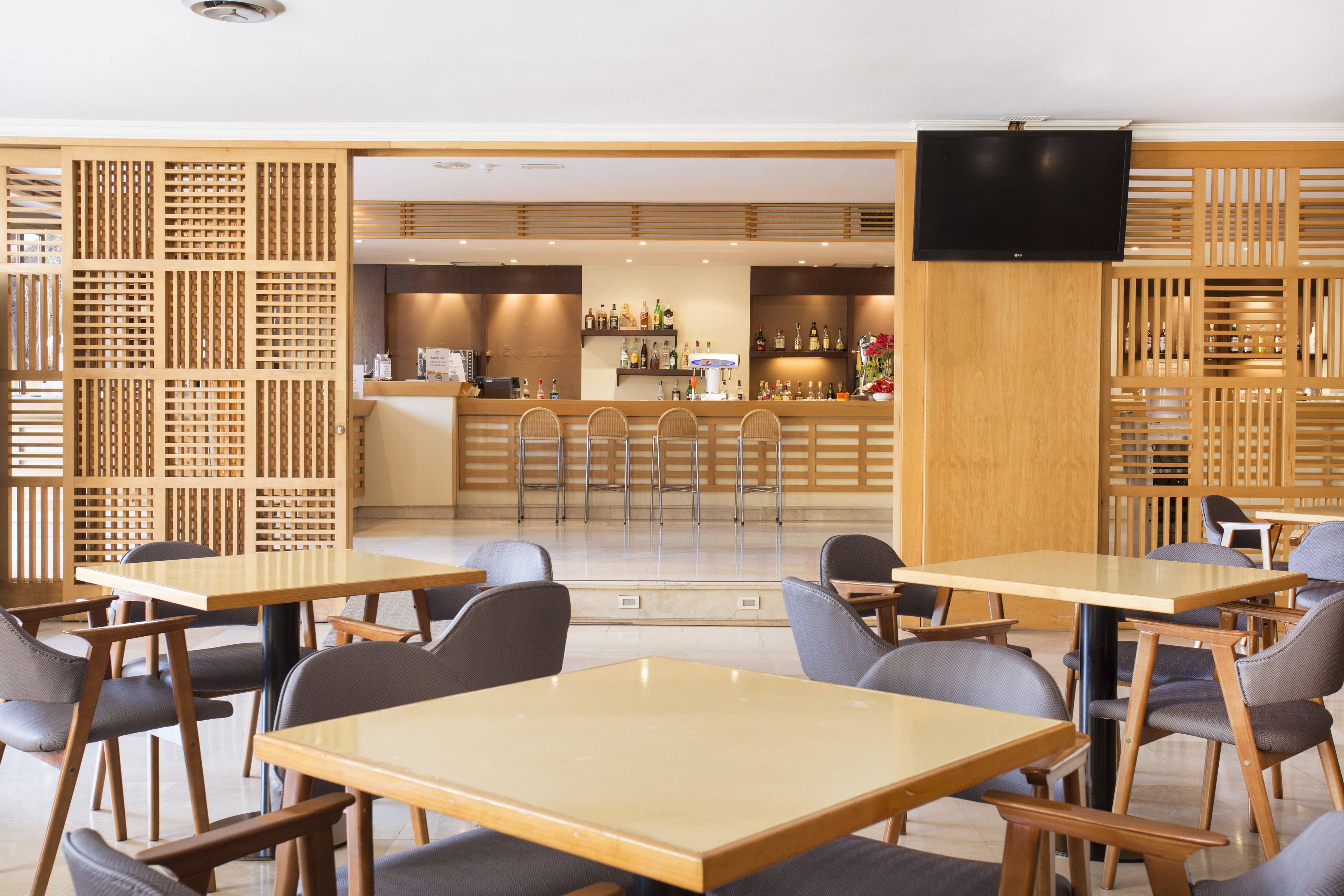 Un ristorante moderno con arredamento in legno, un'area bar e un televisore a schermo piatto.