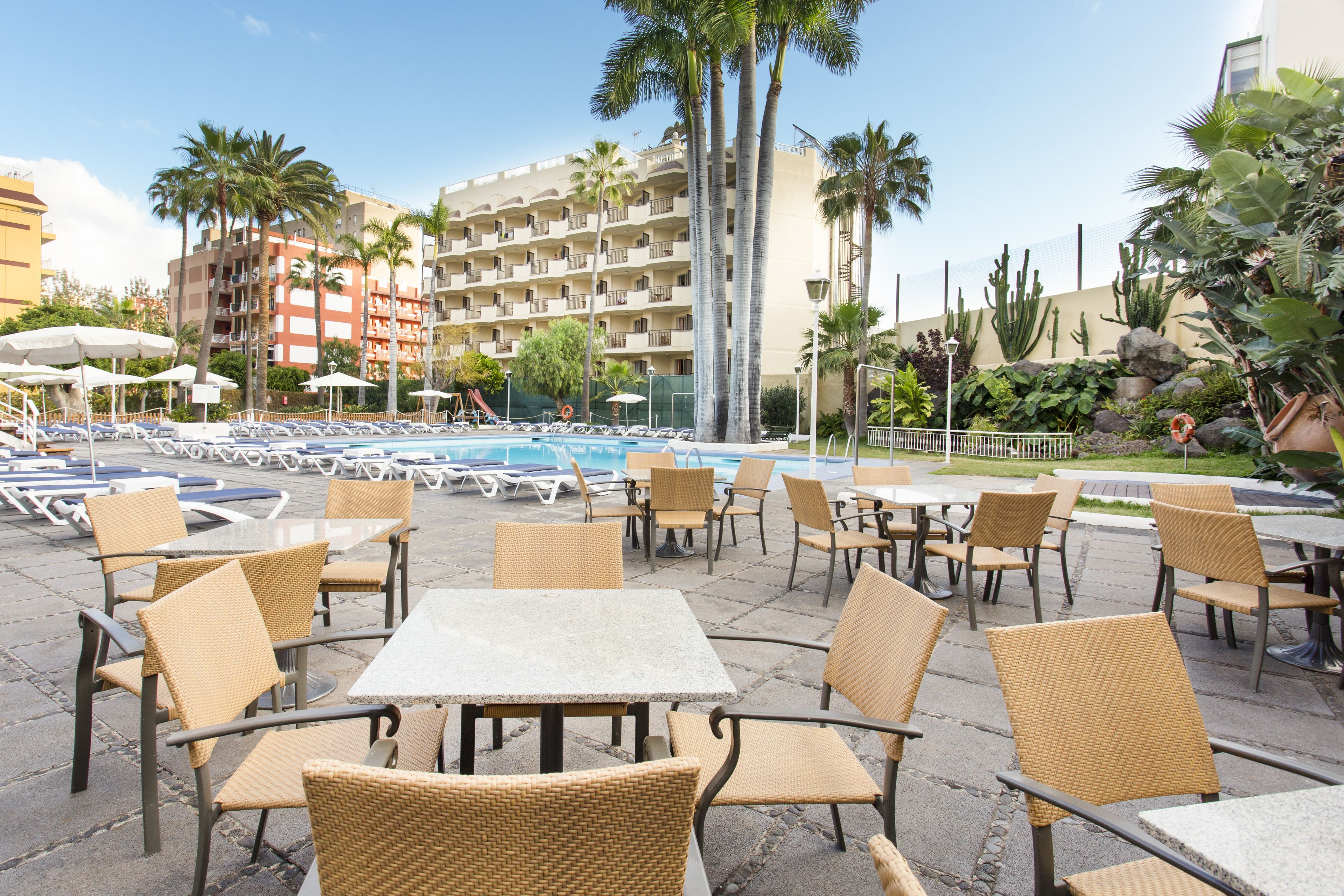 Un espace aménagé au bord de la piscine, avec des chaises longues, des tables et une piscine.