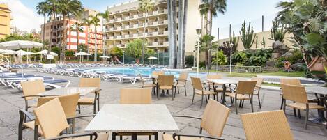Un espace aménagé au bord de la piscine, avec des chaises longues, des tables et une piscine.