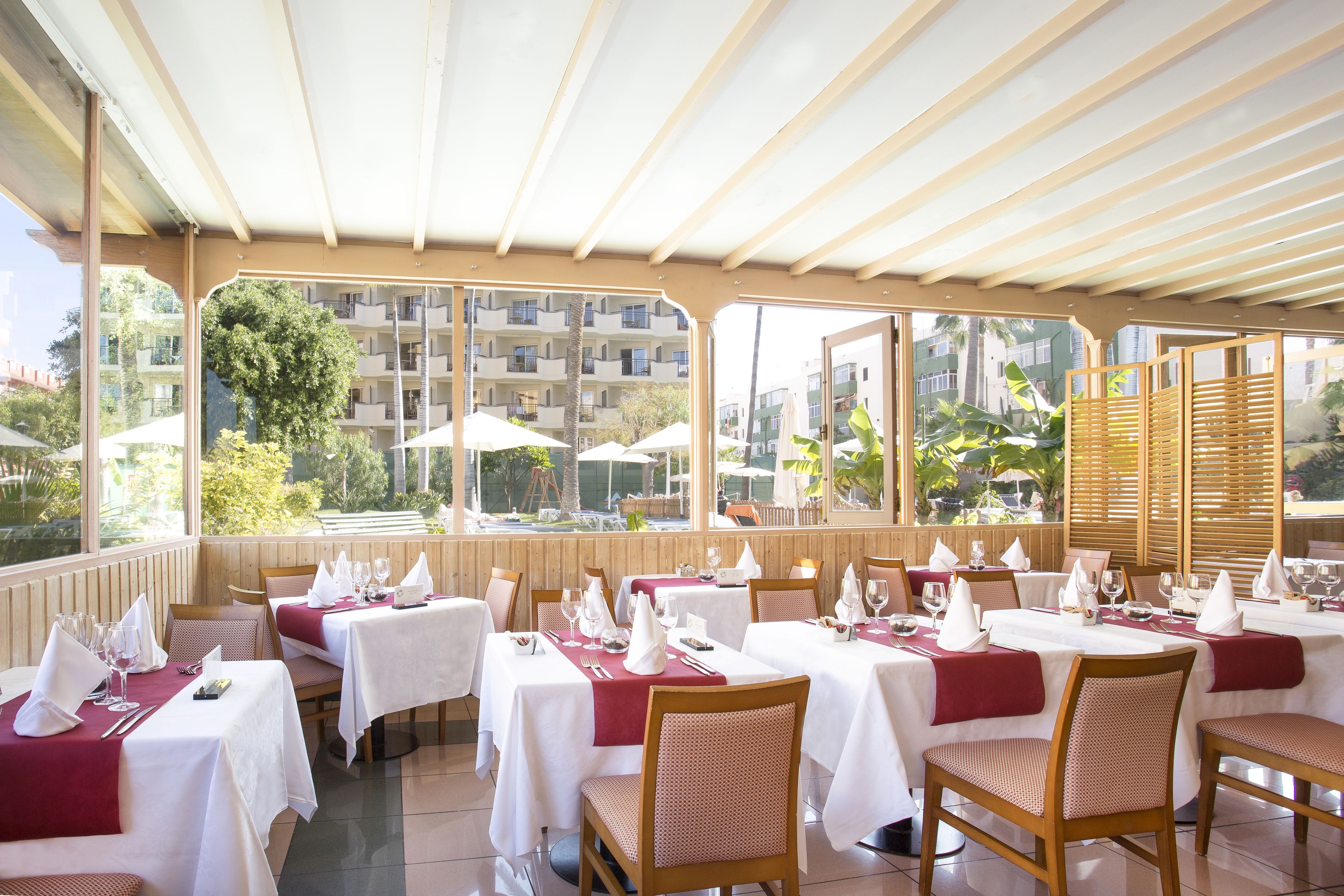 Un restaurante con mesas dispuestas para comer, ventanas amplias y vistas a edificios y árboles.