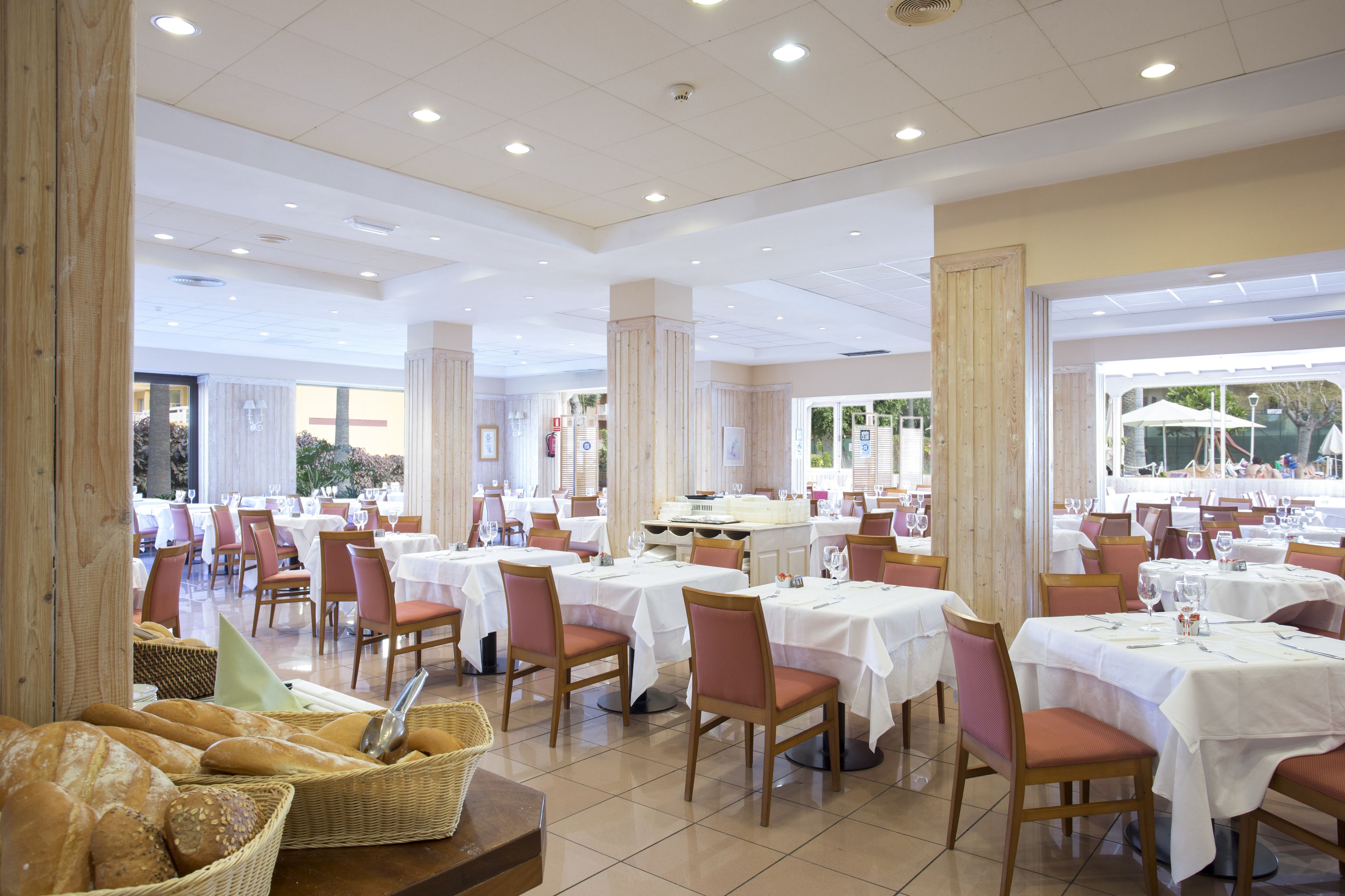 A spacious dining area with multiple tables and chairs, large windows, and a view of the outdoors.