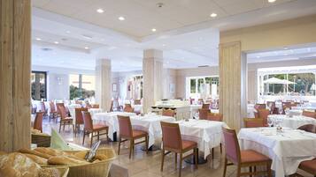 A spacious dining area with multiple tables and chairs, large windows, and a view of the outdoors.