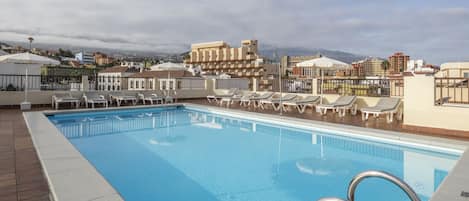 Una piscina en la azotea con sillas de descanso y vistas a la ciudad.
