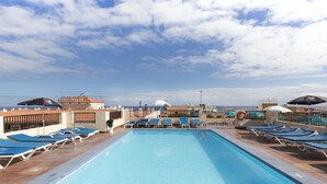 Un área de piscina en la azotea con sillones reclinables azules y sombrillas, vista despejada del océano y un cartel que dice 'Apartamentos Florida Plaza'.