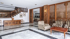 Un vestíbulo amplio con suelo de mármol, una escalera de madera y sillones a rayas.