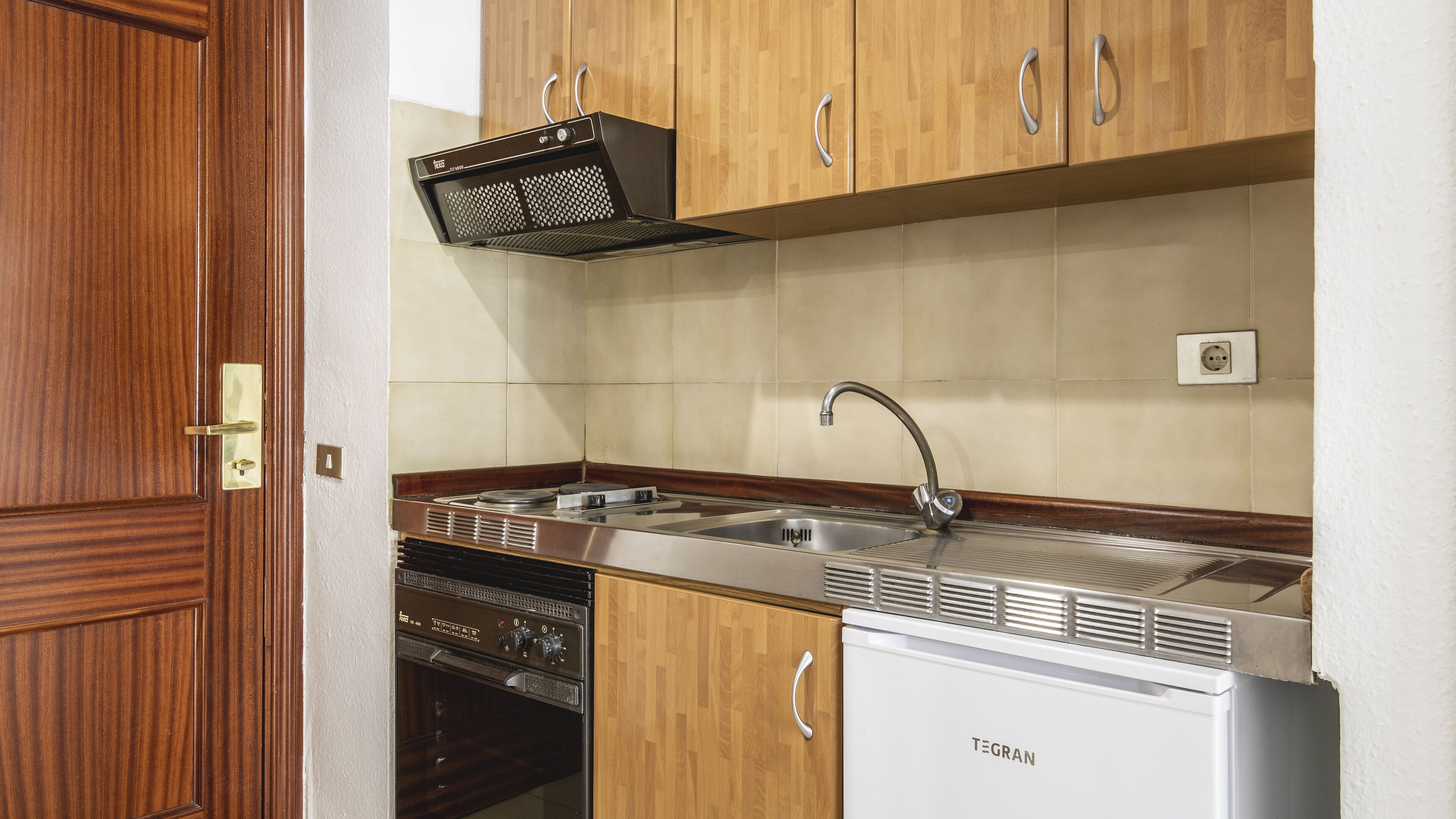 Cuina amb armaris de fusta, un vàter d'acer inoxidable i un rentaplats integrat.