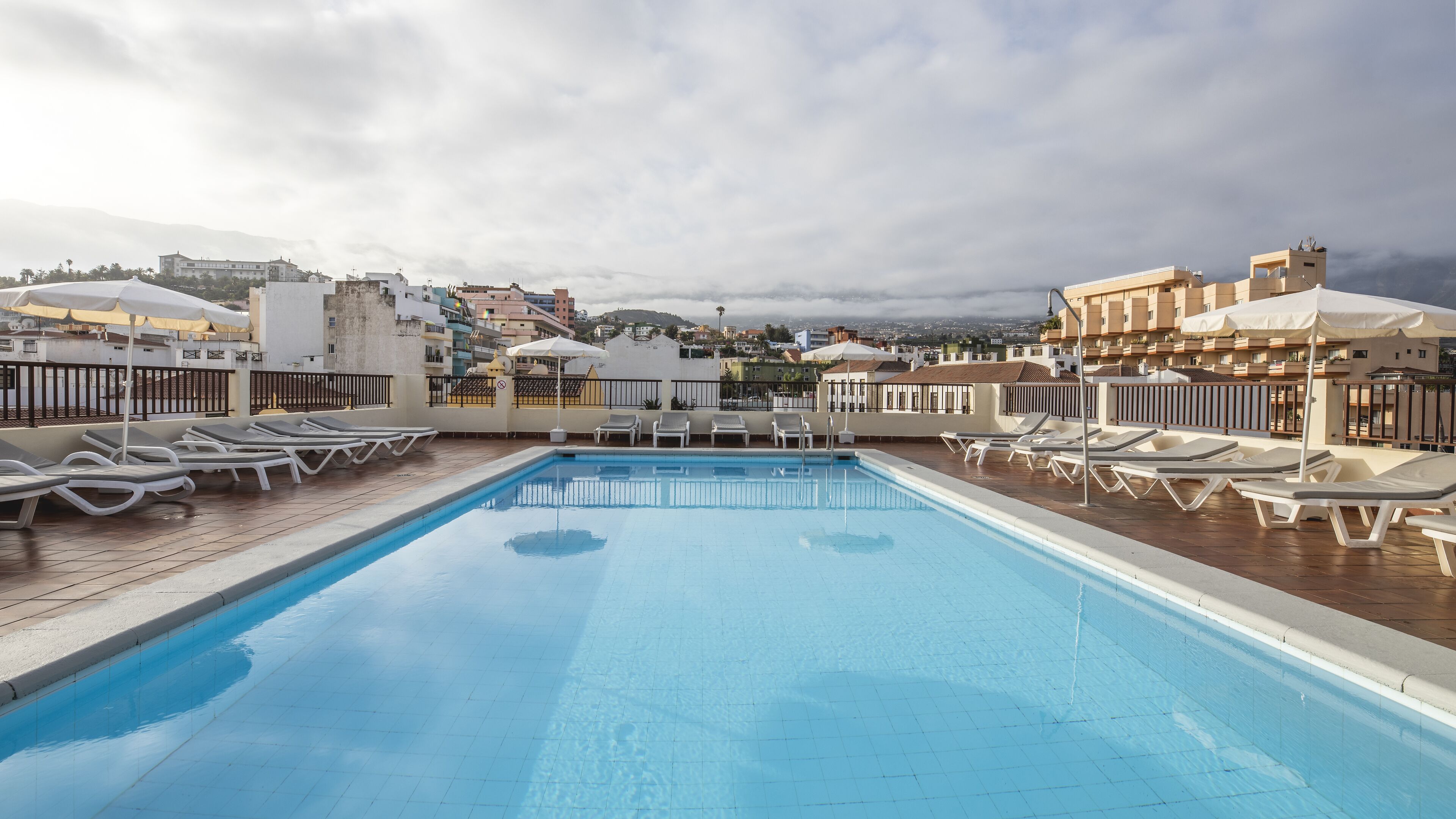 Une piscine sur le toit, dotée de chaises longues et de parasols, entourée d’immeubles et offrant une vue sur la ville.