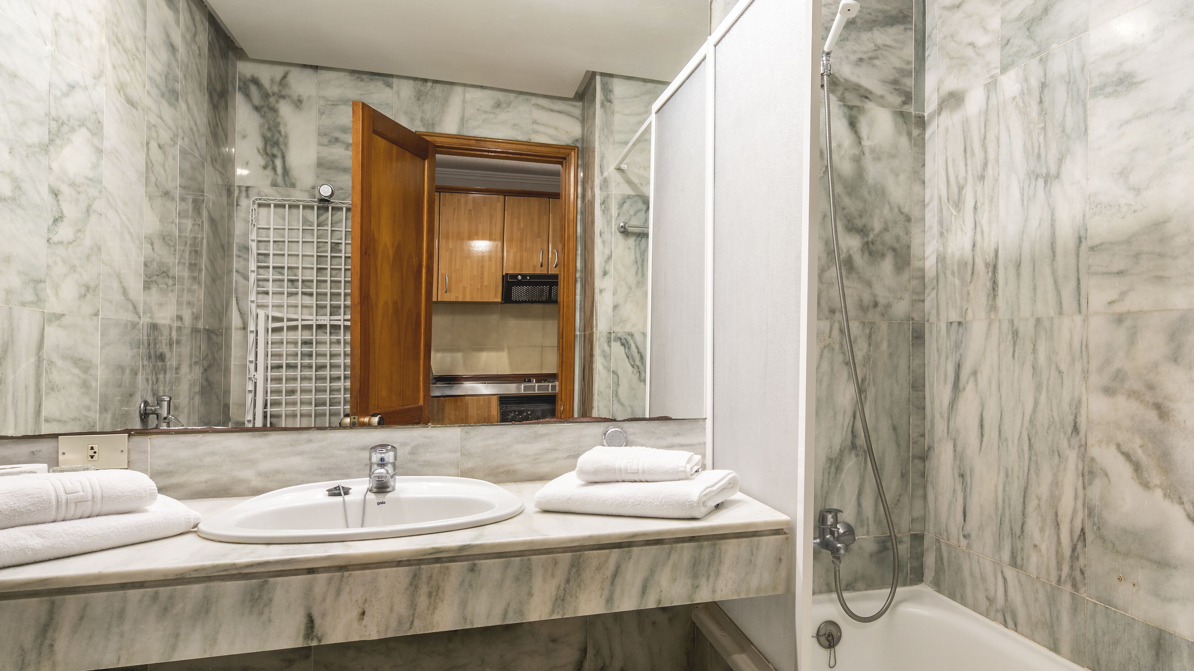 Un bagno con pareti in marmo, un lavabo con specchio e una doccia.