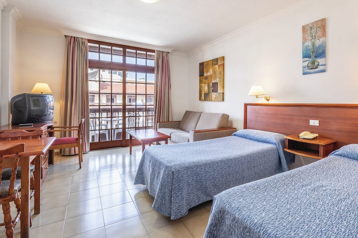 A hotel room with two beds, a desk with a television, a chair, a window with curtains, and a painting on the wall.