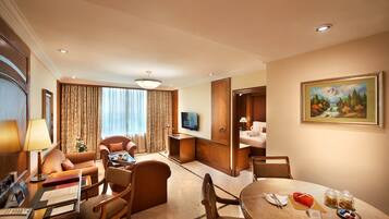 A hotel room with a living area, a dining table with a cake, a TV, and a painting on the wall.
