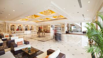 A spacious lobby with a marble floor, comfortable seating areas, and a central chandelier.