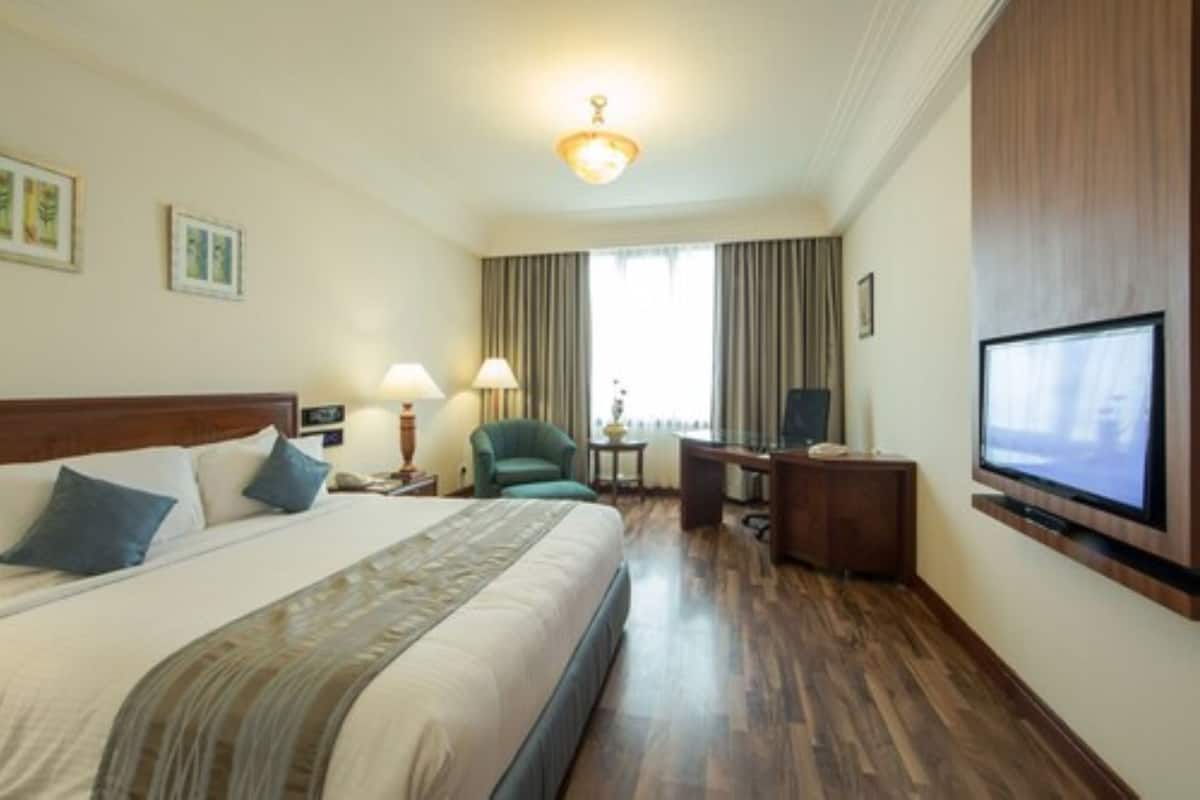 Una habitación de hotel con una cama grande, un escritorio con silla, televisión y ventana con cortinas.