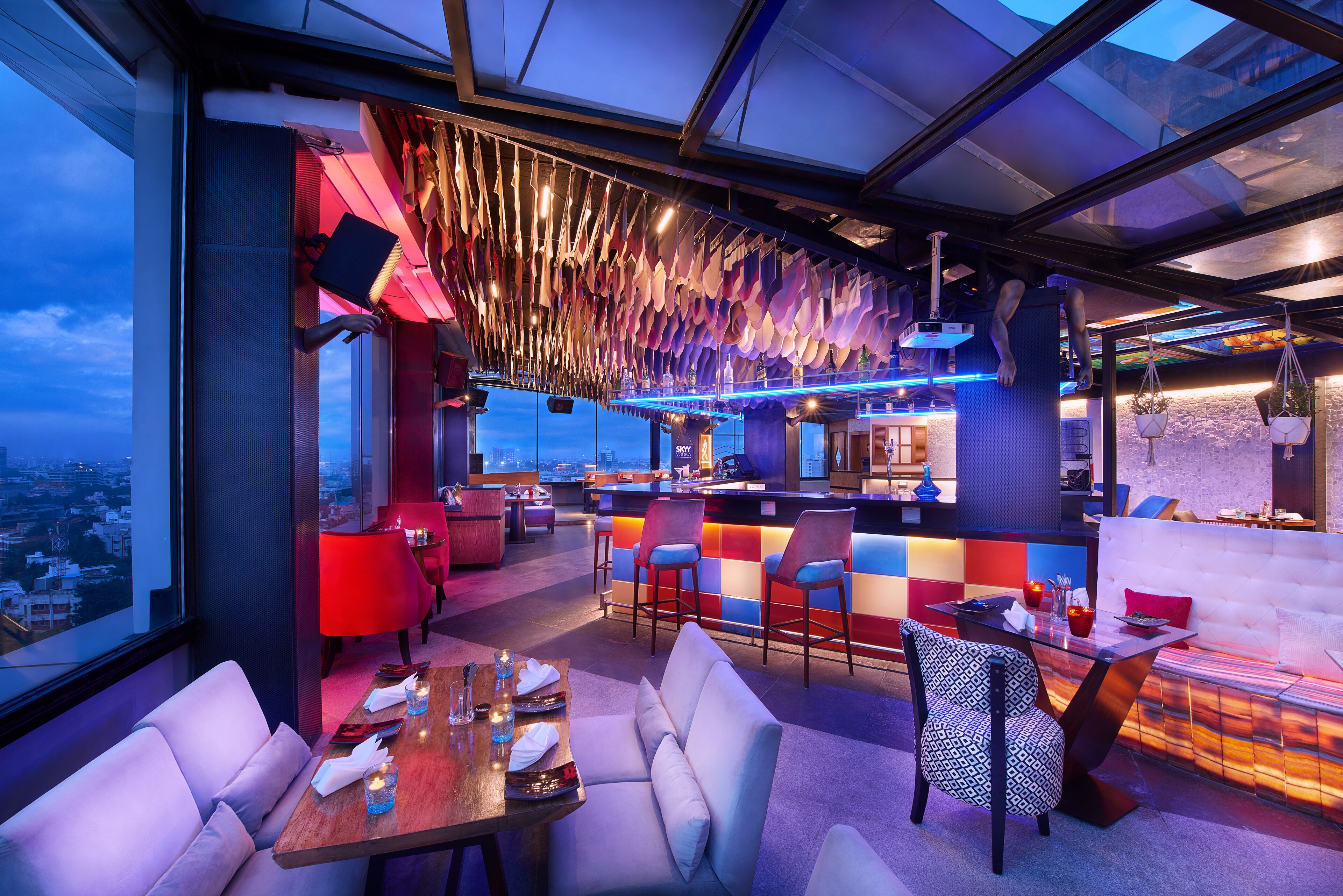 A modern restaurant with a bar area, seating arrangements, and a view of the cityscape.