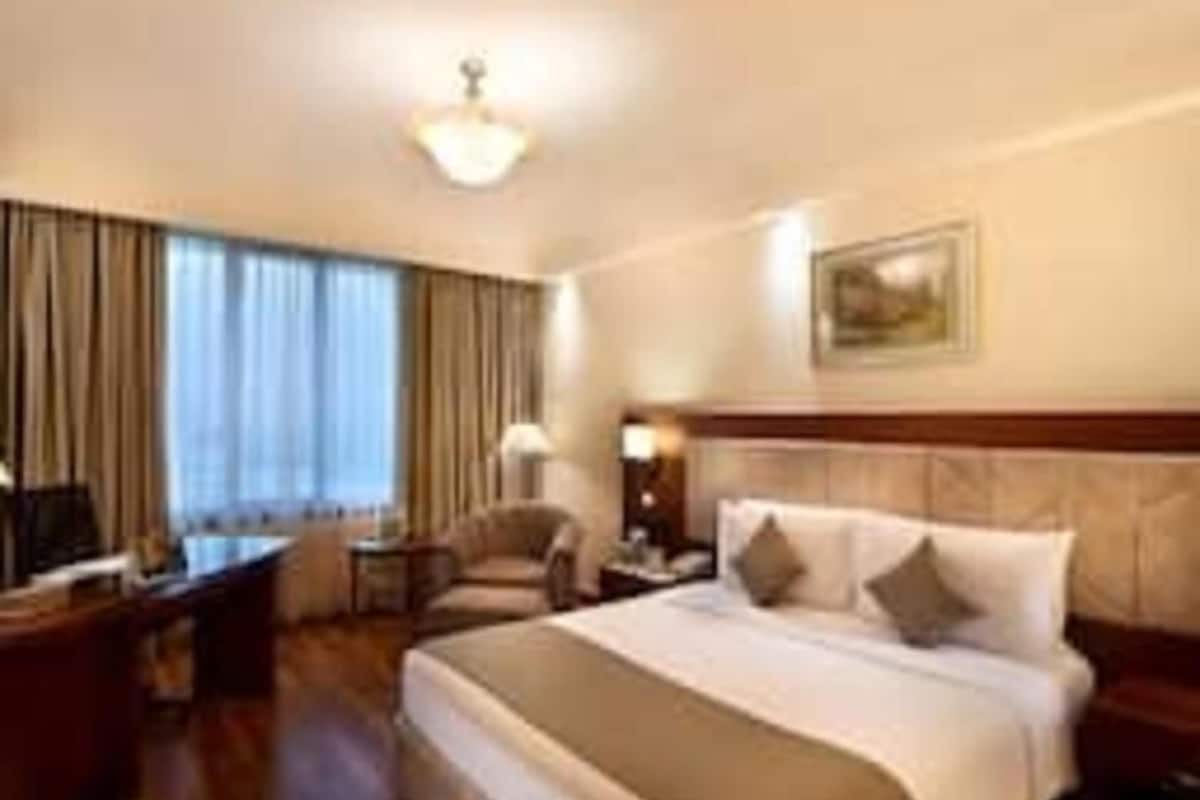 Una habitación de hotel con cama, escritorio, silla, lámpara y un cuadro en la pared.