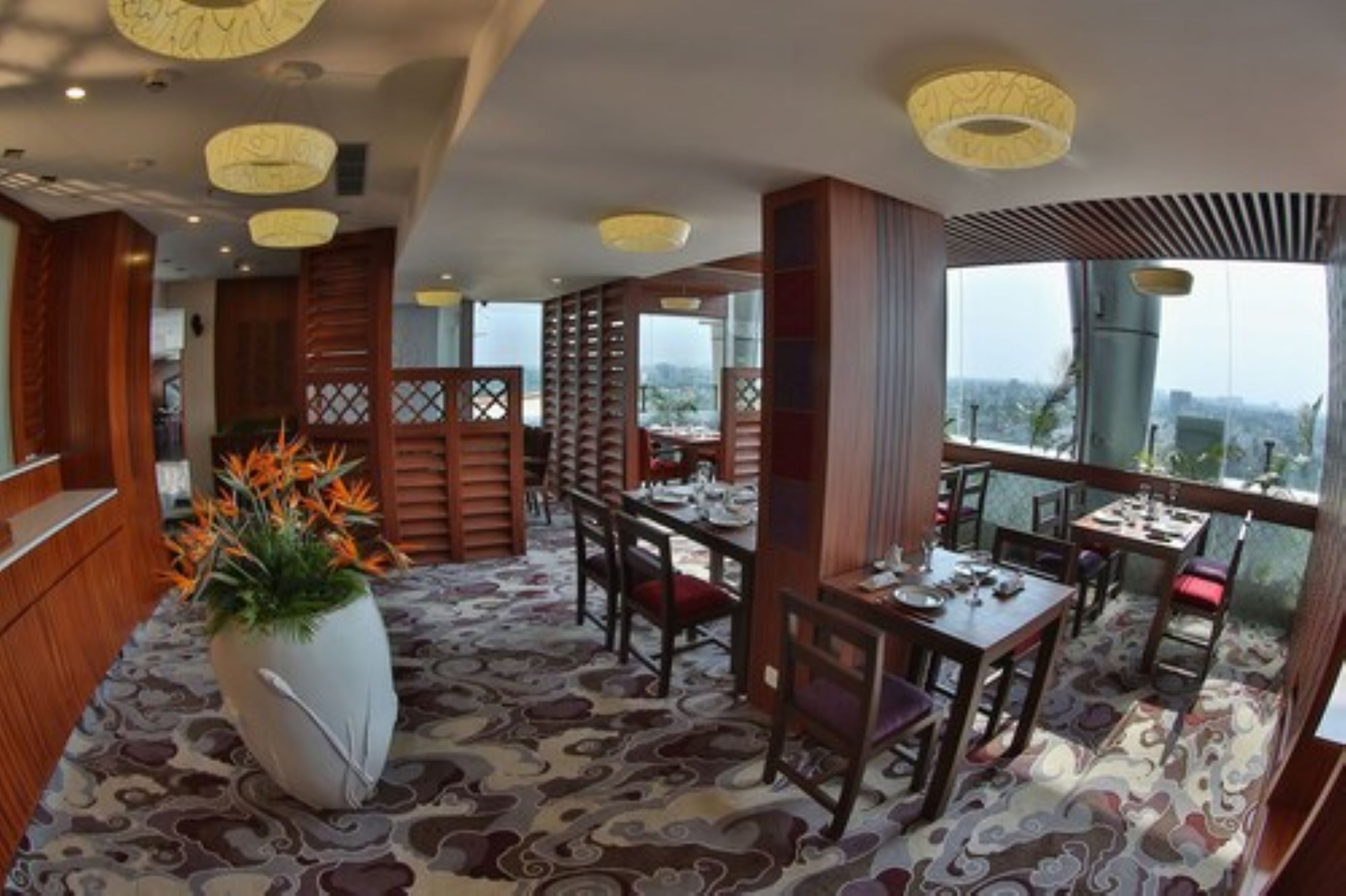 Un restaurante con mobiliario de madera, un jarrón grande con flores y una alfombra estampada.