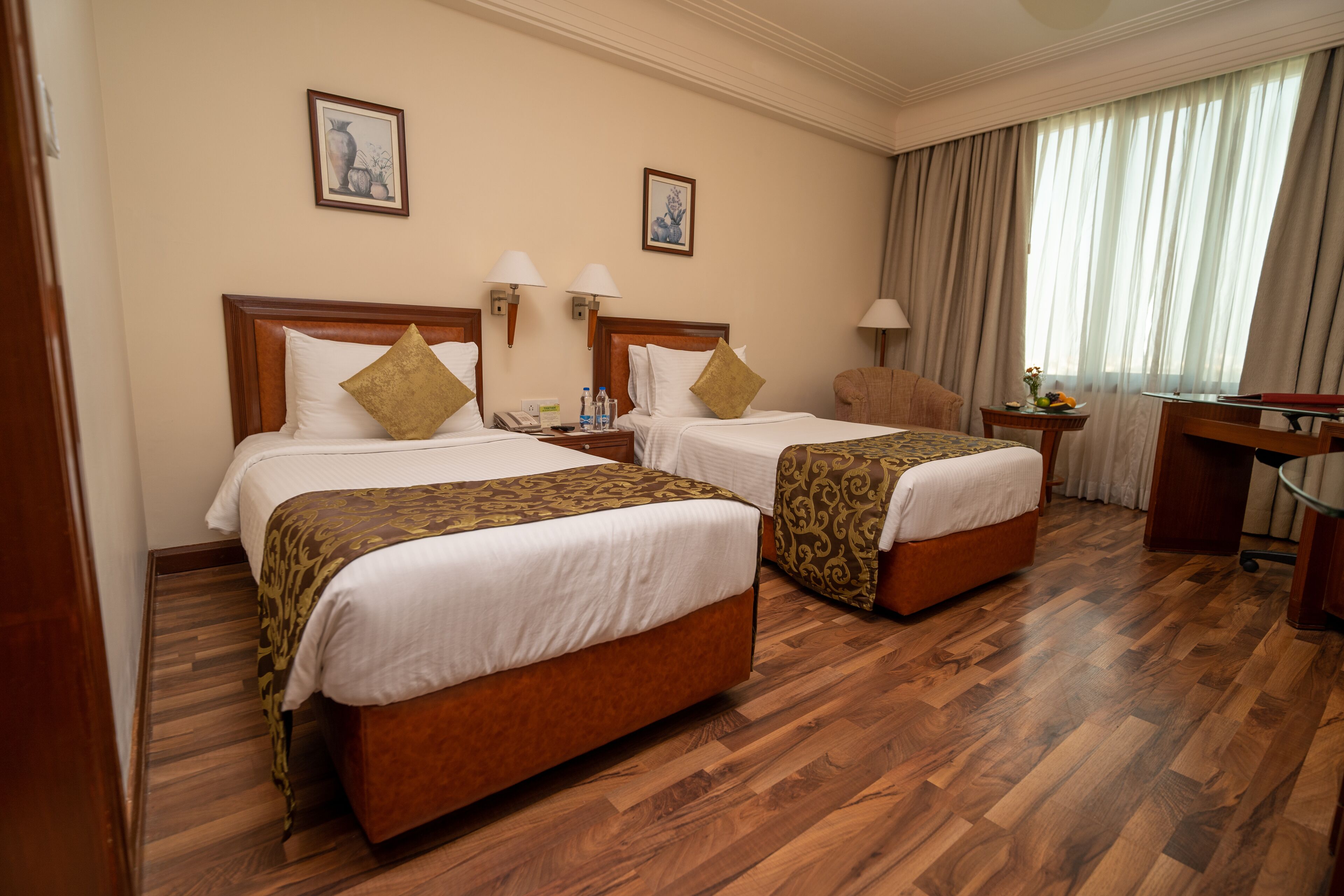 A hotel room with two beds, wooden flooring, a desk, and a chair.