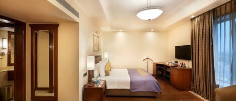 Habitación de hotel con cama, mesita de noche, lámpara, televisor y una zona de estar con sofá y mesa de centro.