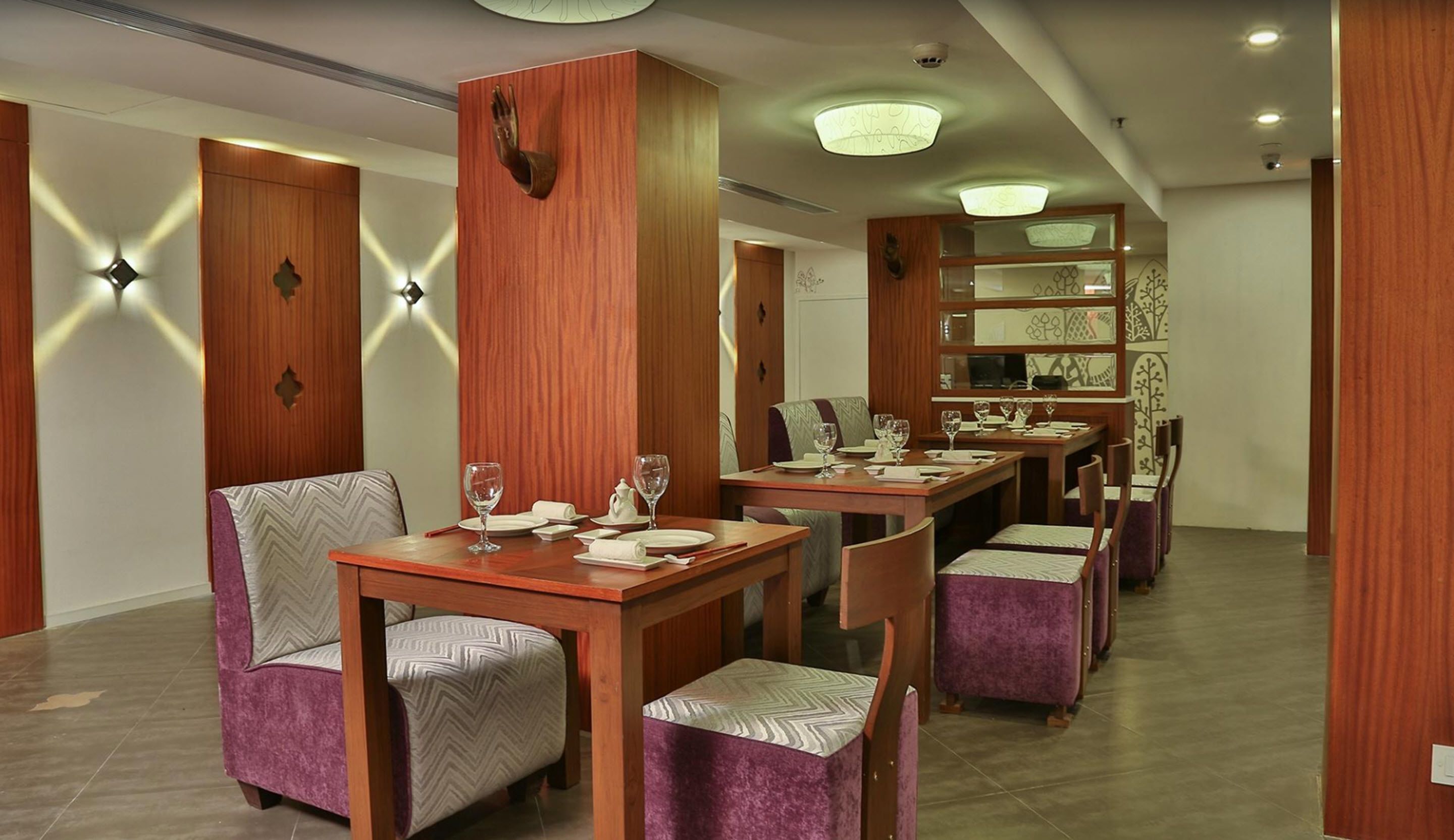 A dining area with wooden tables and purple upholstered chairs, featuring a modern chandelier and decorative wall sconces.