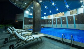 A swimming pool area with lounge chairs, a covered seating area, and a poolside bar. - The Accord Metropolitan (Chennai)