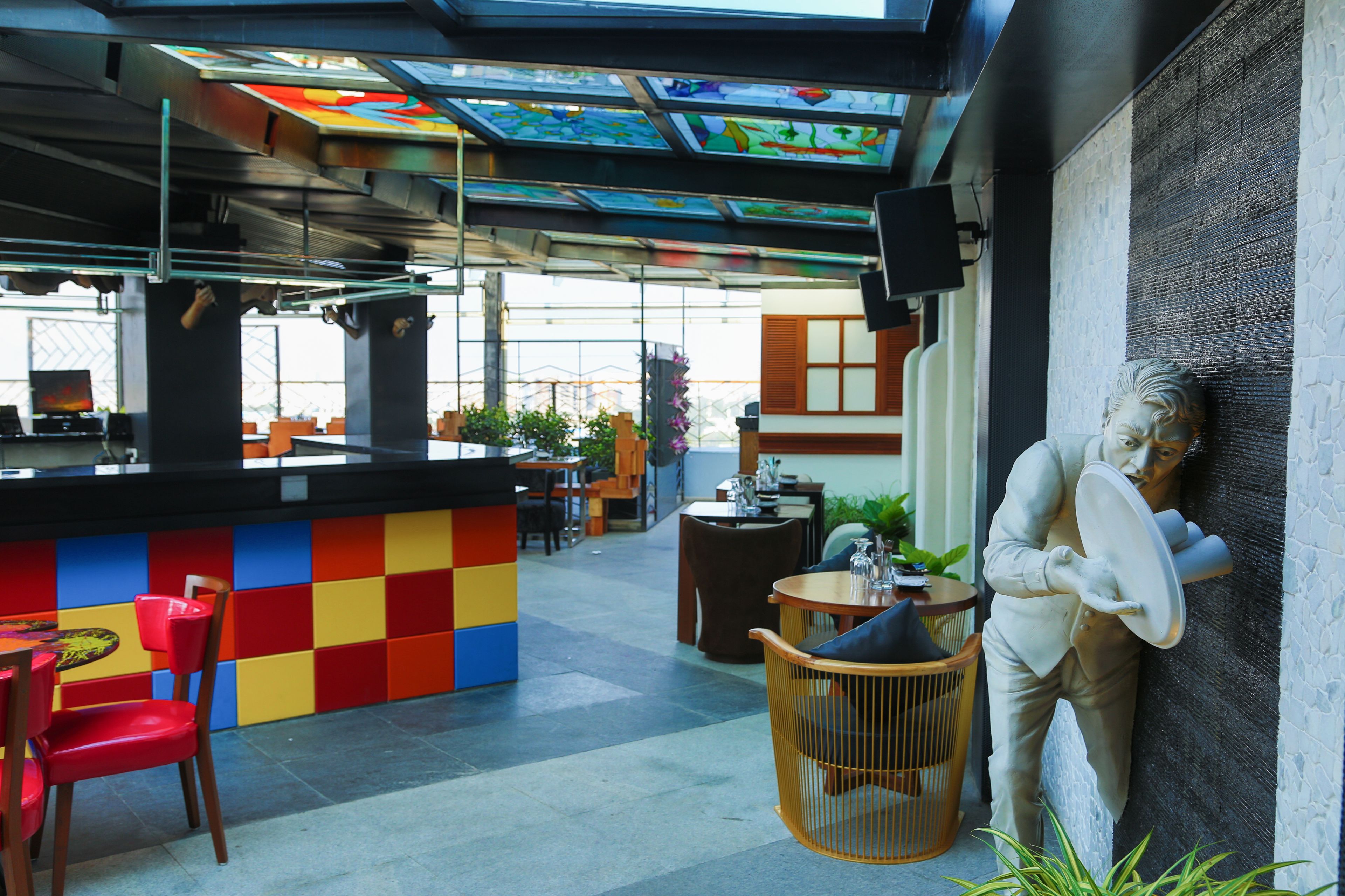 A modern interior with a colorful checkered wall, a bar area, and a statue of a man holding a plate.