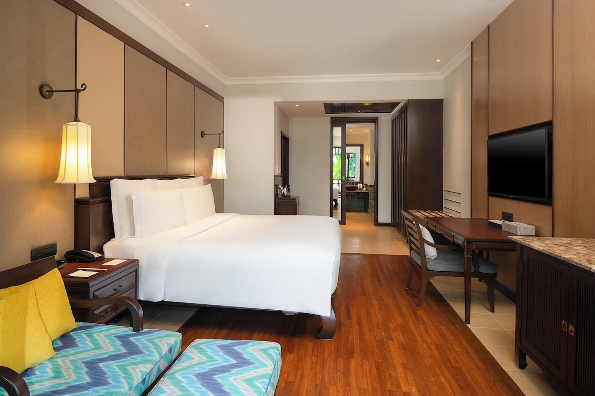 A hotel room with a bed, bedside table, lamp, desk, chair, and TV.