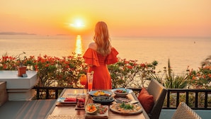 A woman dining at a table with a view of the sunset over the water. - InterContinental Pattaya Resort by IHG (Pattaya)
