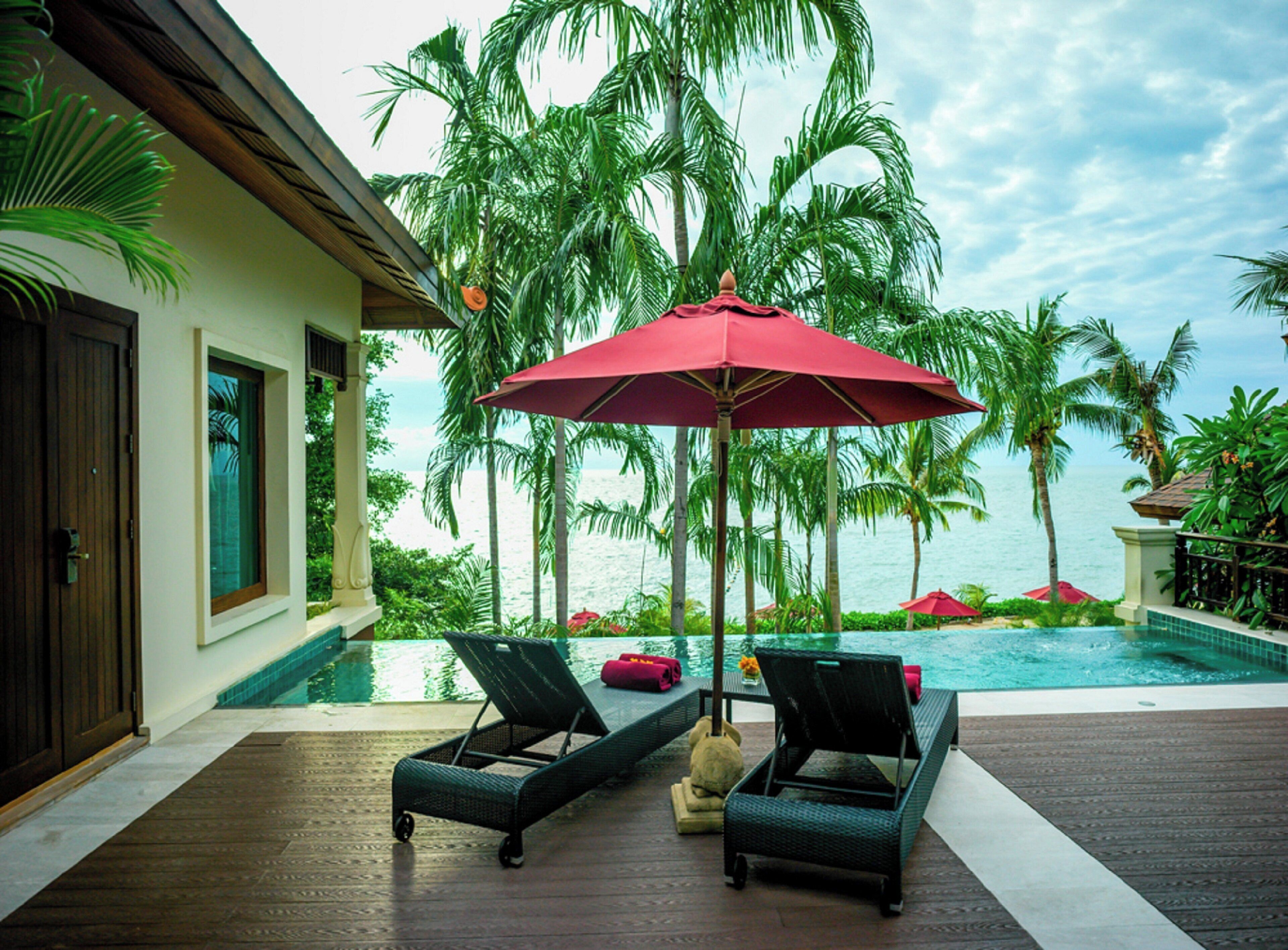 A poolside area with lounge chairs, a red umbrella, and a view of the ocean.