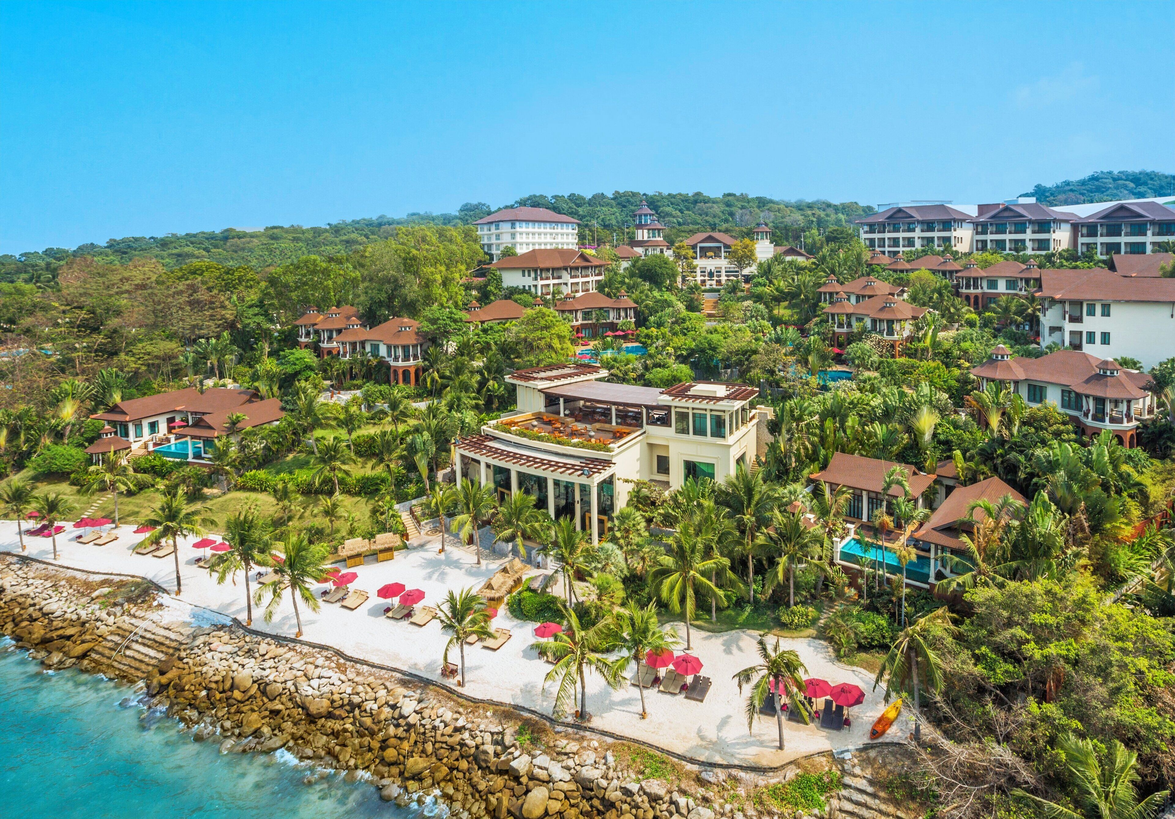 A resort with multiple buildings, a pool, and a beach area with umbrellas and lounge chairs.