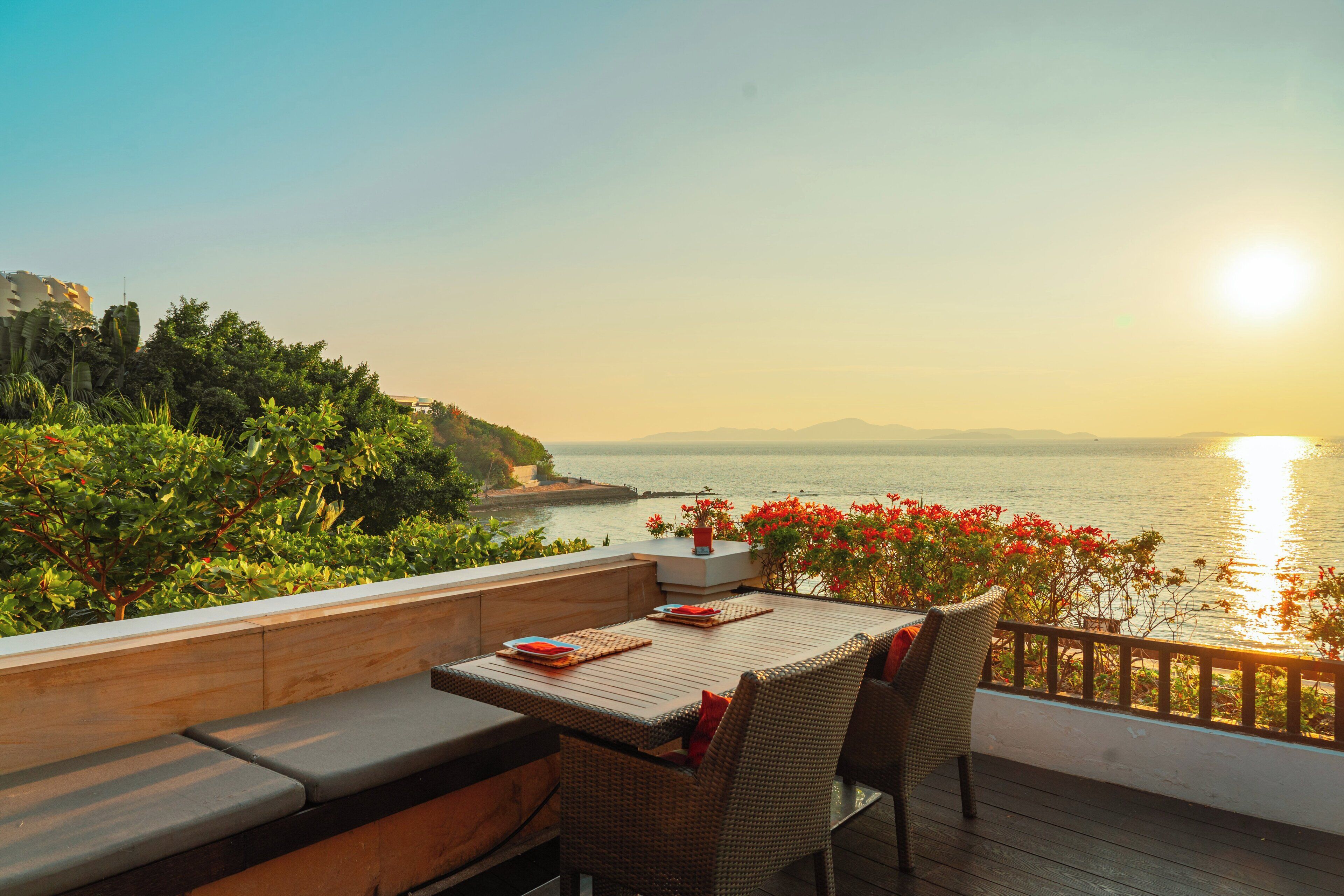 A terrace with a table and chairs, overlooking a body of water and a distant mountain range.