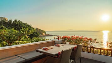 A terrace with a table and chairs, overlooking a body of water and a distant mountain range.