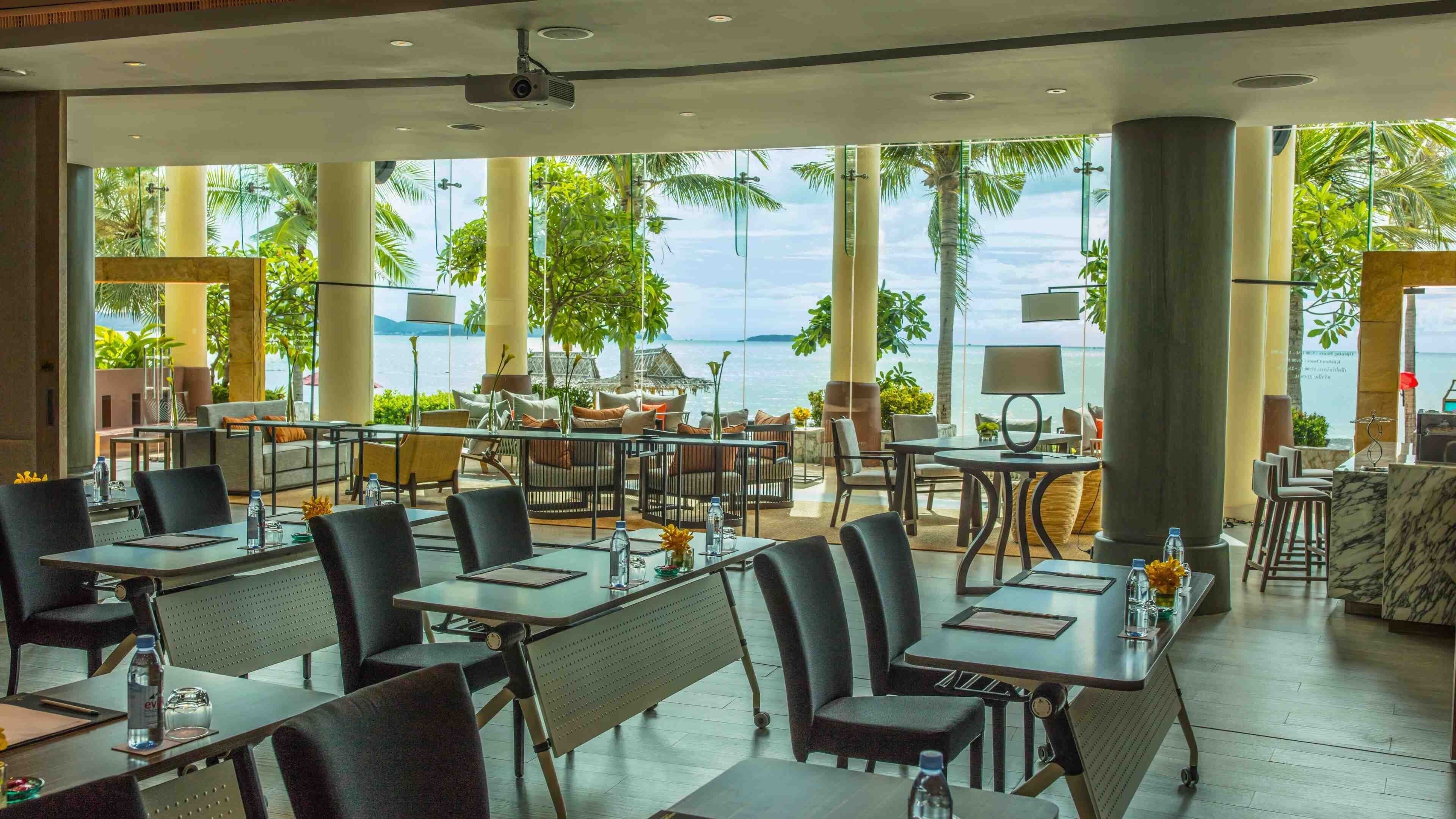 Un restaurant moderne avec des tables et des chaises, de grandes fenêtres et une vue sur la mer.
