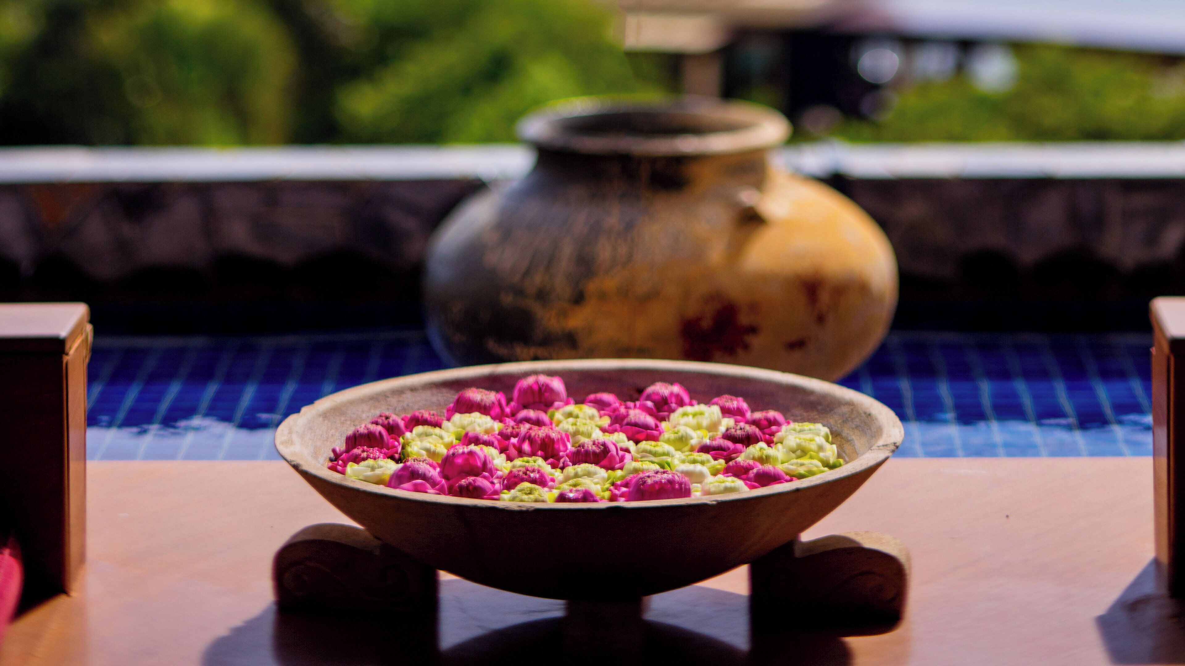 A bowl of colorful flowers on a wooden table with a blurred background.