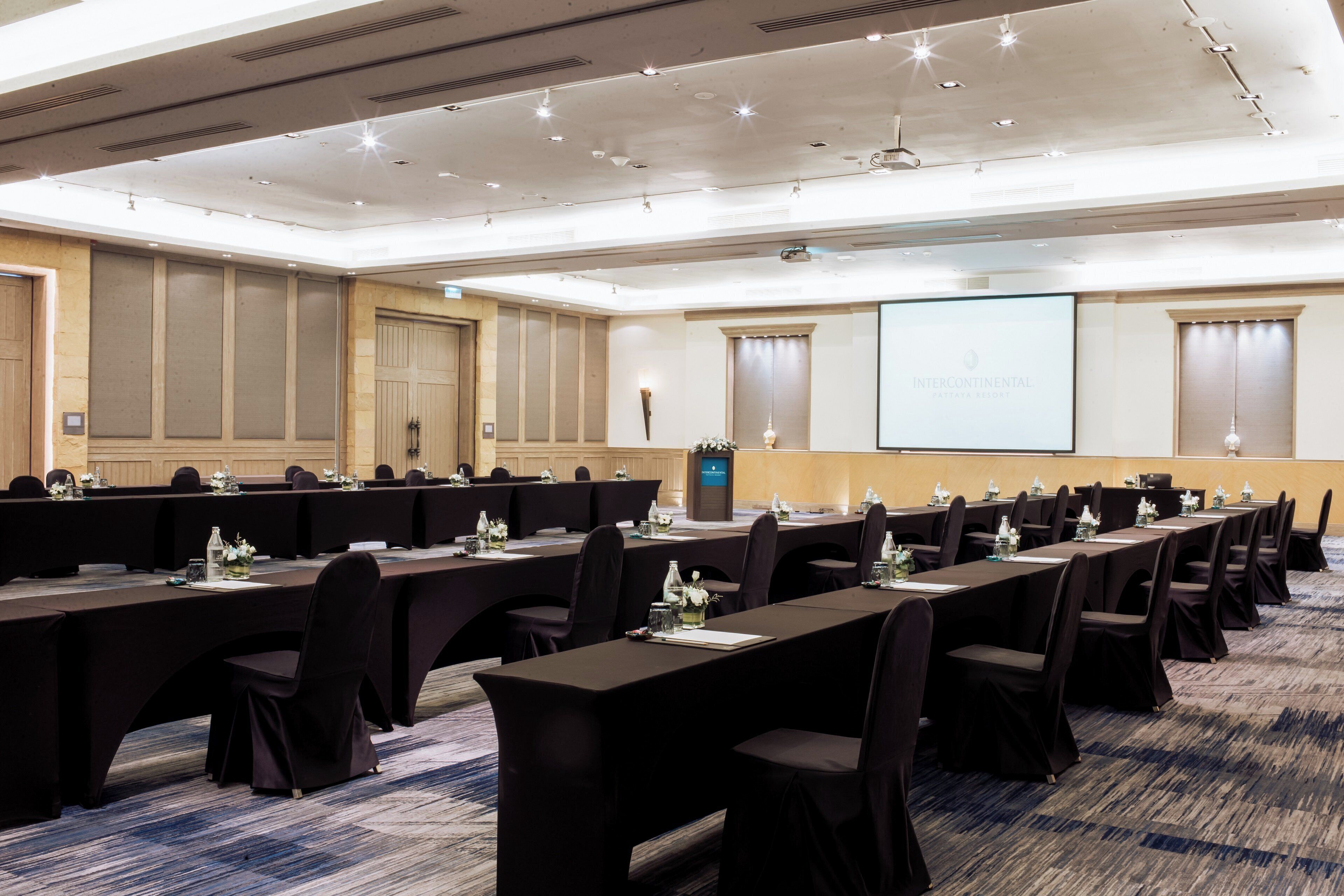 Une salle de conférence équipée de longues tables, de chaises et d’un écran de projection affichant le mot « INTERCONTINENTAL ».