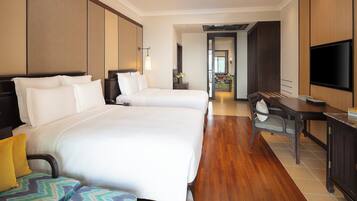Quarto de hotel com duas camas, uma escrivaninha, uma cadeira, televisão e vista para a varanda.