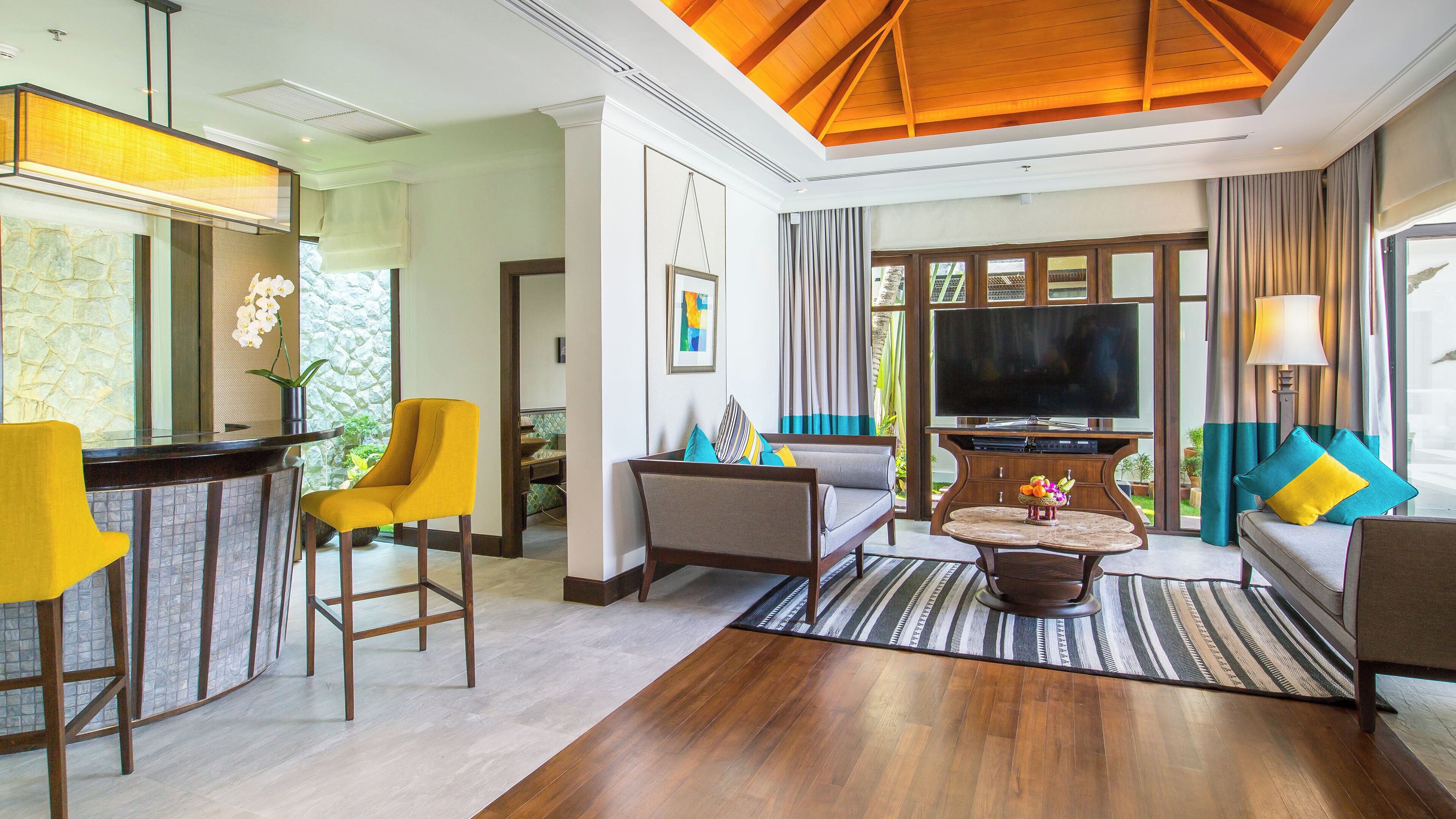 A modern living room with a wooden ceiling, a flat-screen TV, and a seating area with a sofa and armchairs.