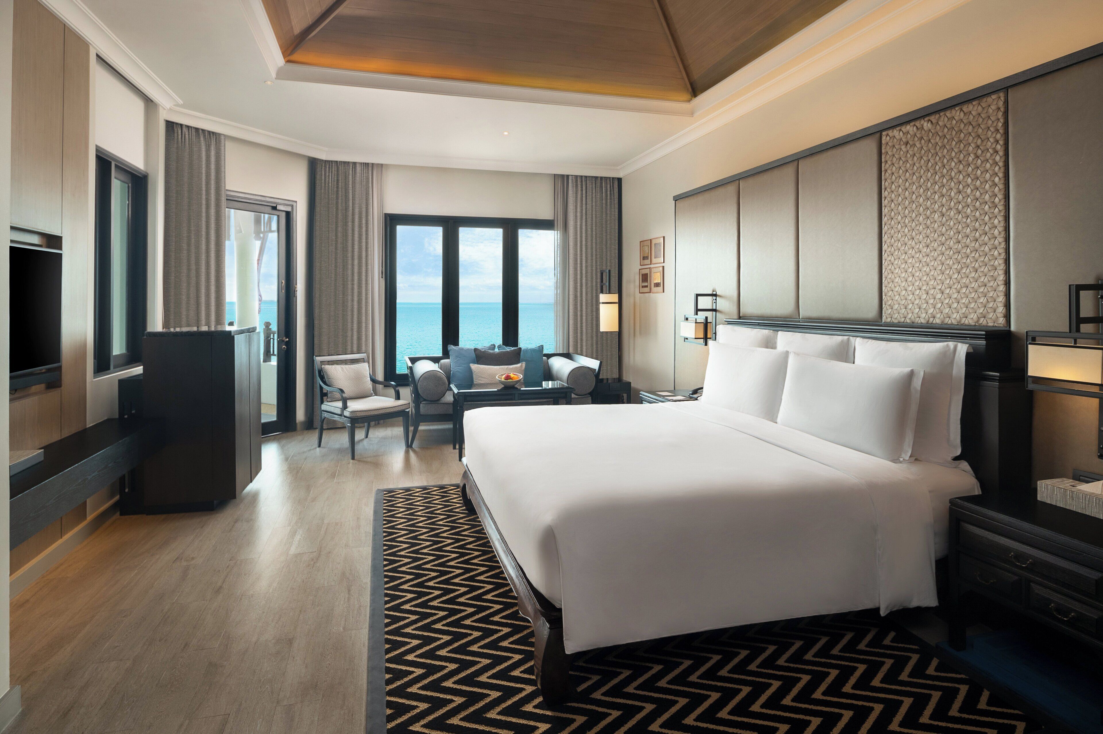 Ein Hotelzimmer mit einem großen Bett, einem Schreibtisch, einem Sessel, einem Fernseher und Meerblick.