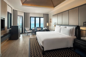 Habitación de hotel con una cama grande, un escritorio, una silla, un televisor y vistas al mar.