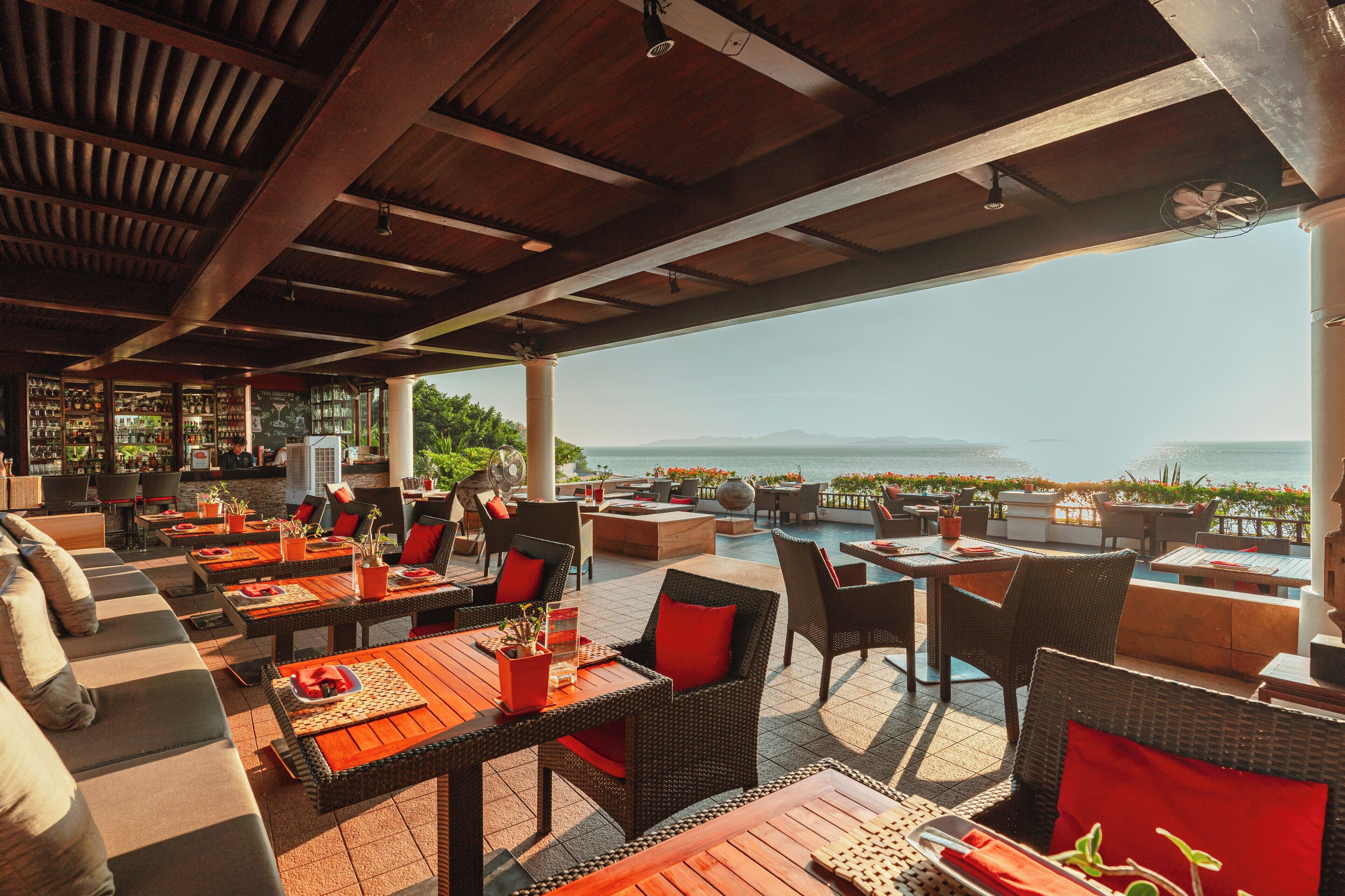 An outdoor seating area with tables and chairs, a pool, and a view of the sea.